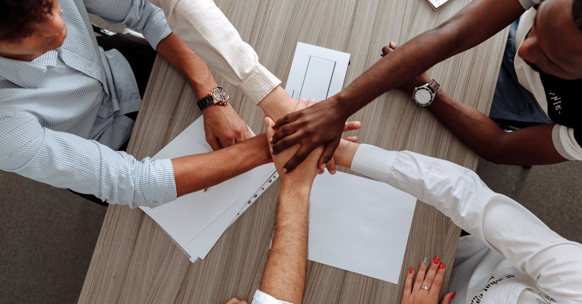 A diverse group of adults join hands in an office, symbolizing teamwork and cooperation.